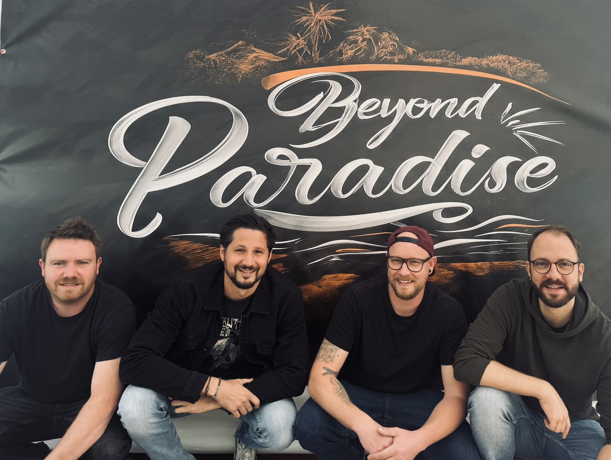 Die vier Mitglieder von Beyond Paradise gemeinsam vor ihrem Bandbanner